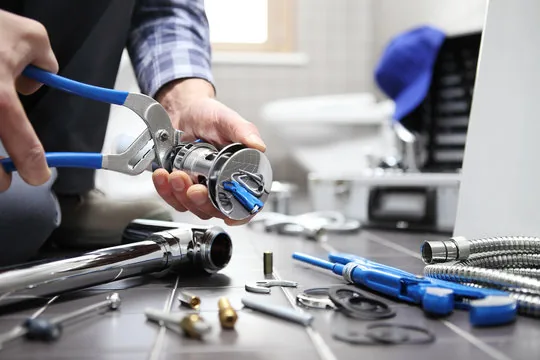 Plumber using pliers to replace a faucet cartridge, with tools and parts on the counter