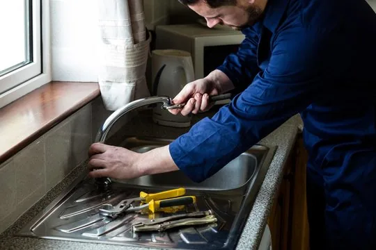 Loveland plumber tightening a kitchen faucet with an adjustable wrench, tools laid on the sink